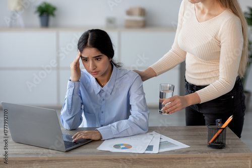 фотографія A millennial Indian woman sits at her workplace, showing signs of stress and discomfort from a headache