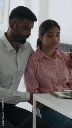 Vertical video loving indian husband supports and consoles distressed wife during a tense medical consultation, showing care and empathy