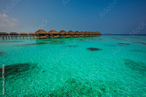 Fototapeta Naklejka Na Ścianę i Meble -  Tranquil closeup calm sea water waves with palm trees. Bungalows background. Tropical island beach landscape exotic shore coast. Summer vacation, holiday amazing nature. Relax paradise, Maldives.