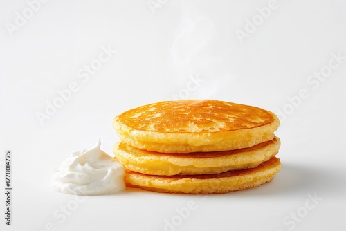Golden stack of pancakes with a side of white creamy topping on a plain white background.
