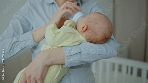A young attractive brunette woman is feeding a baby formula to a breastfed baby unrecognizable. The concept of artificial quality feeding
