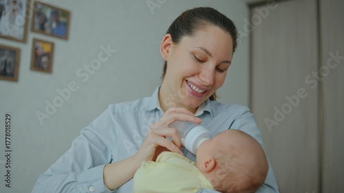  A young attractive brunette woman is feeding a baby formula to a breastfed baby. The concept of artificial quality feeding