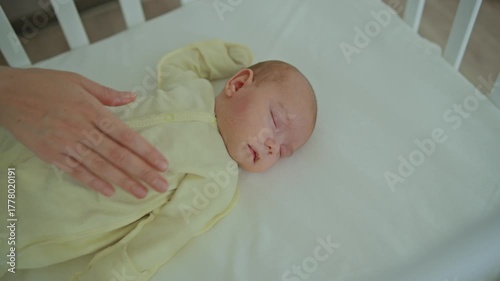 A mother gently strokes a one-month-old baby who is sleeping in a white wooden crib
