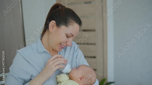  A young attractive brunette woman is feeding a baby formula to a breastfed baby. The concept of artificial quality feeding