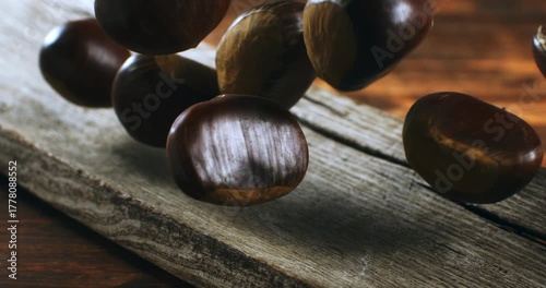Slow motion macro of autumn chestnuts falling on rustic wood surface. Cozy, seasonal and organic atmosphere at 1000 fps.