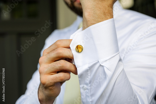 Close-up of a man adjusting his elegant white shirt cuff with a stylish golden cufflink. Concept of luxury fashion, men’s style, formal wear, and attention to detail
