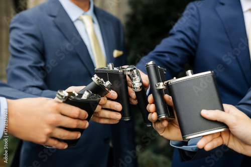 Slika na platnu Group of men in elegant suits making a toast with black leather flasks