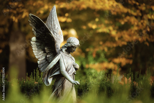 Side view of a serene bronze angel statue with detailed wings and bowed head, set against a bright, golden yellow autumn foliage bokeh