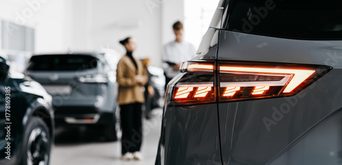 Modern car dealership interior showcasing sleek vehicles with a focus on a gray car's rear lights, highlighting the vibrant atmosphere of automotive sales and customer engagement