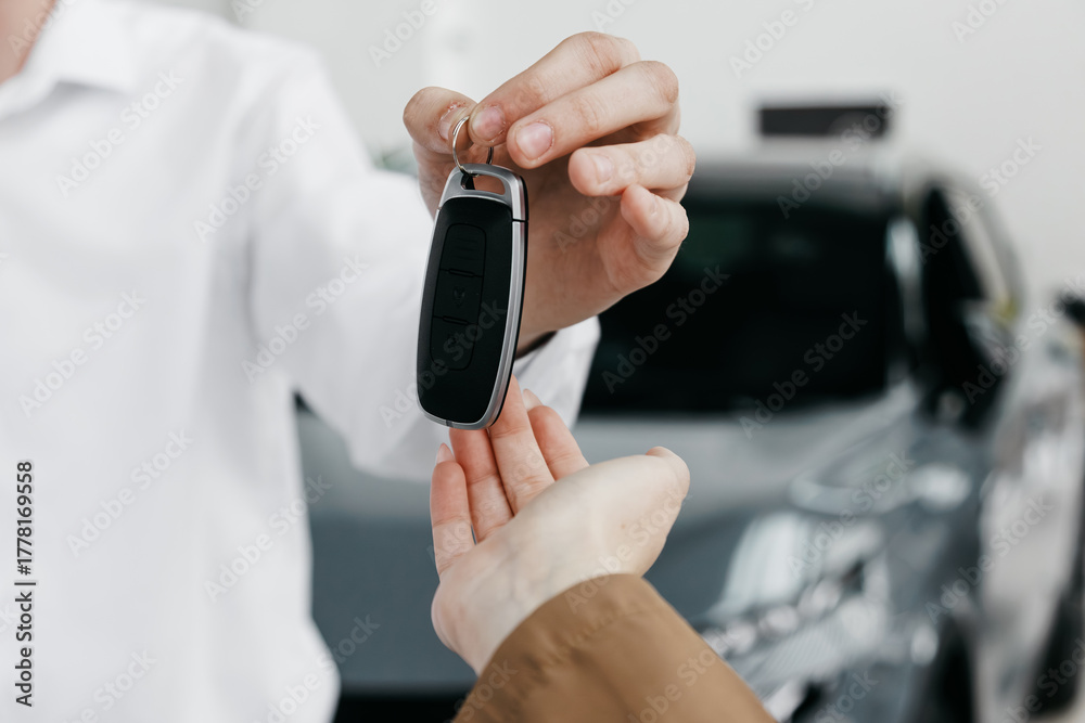 Fototapeta premium Man in white shirt handing over car keys to customer, showcasing successful car sale transaction in modern dealership environment with vehicles in background