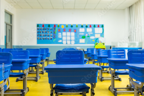 Empty classroom with blue desks and colorful bulletin board in modern school
