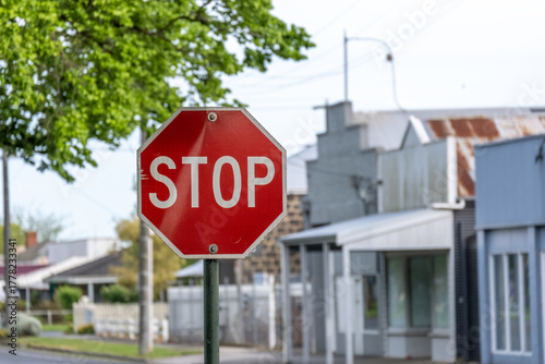 Fototapeta Naklejka Na Ścianę i Meble -  Red STOP sign at a street intersection in a small Australian town, with residential and commercial buildings in the background. Traffic control and road safety in Camperdown, Victoria, Australia.