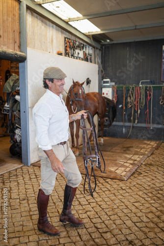 Senior man walking in horse stable with riding gea