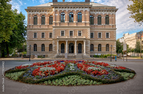 Zagreb, Croatia – July 18, 2025: The Croatian Academy of Sciences and Arts (HAZU) stands behind a circular floral display in Zrinjevac Park.
