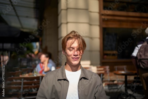 Smiling Young Man Enjoying a Sunny Day at a Bustling Cafe