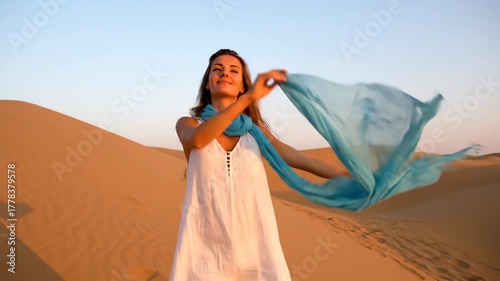 A joyful woman raises her arms with a flowing blue scarf in the vast desert.