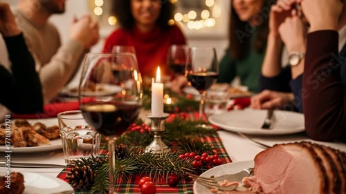 Diverse group of friends and family enjoying a festive holiday dinner with delicious ham, red wine, and beautiful Christmas decorations on a plaid tablecloth
