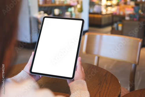 Mockup image of a woman holding digital tablet with blank white desktop screen in cafe
