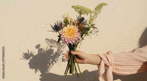 Womans hand holding a bouquet of flowers with shadow on a beige wall