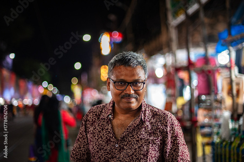 Middle aged Indian man standing on a busy street in a city at night