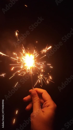 Close-up view of Hand holding sparkling fireworks for night celebration on holiday, new year's eve. Vertical Footage
