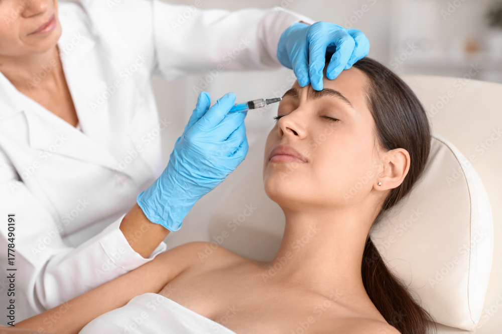 Naklejka premium Young woman receiving forehead filler injection in beauty salon