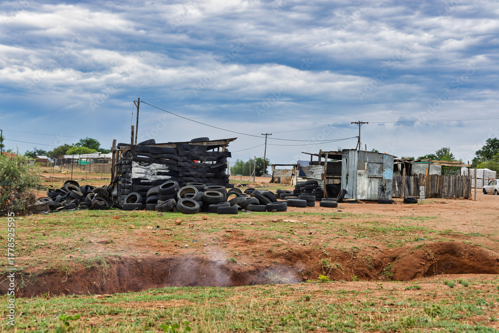 Fototapeta premium informal settlement, or shanty town, built with corrugated iron sheets and discarded tires, makeshift housing and smoking ditch