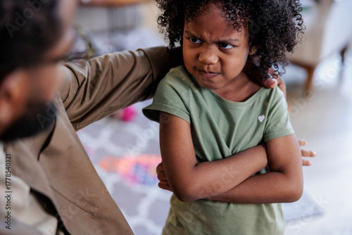 Angry child with crossed arms being comforted by parent.
