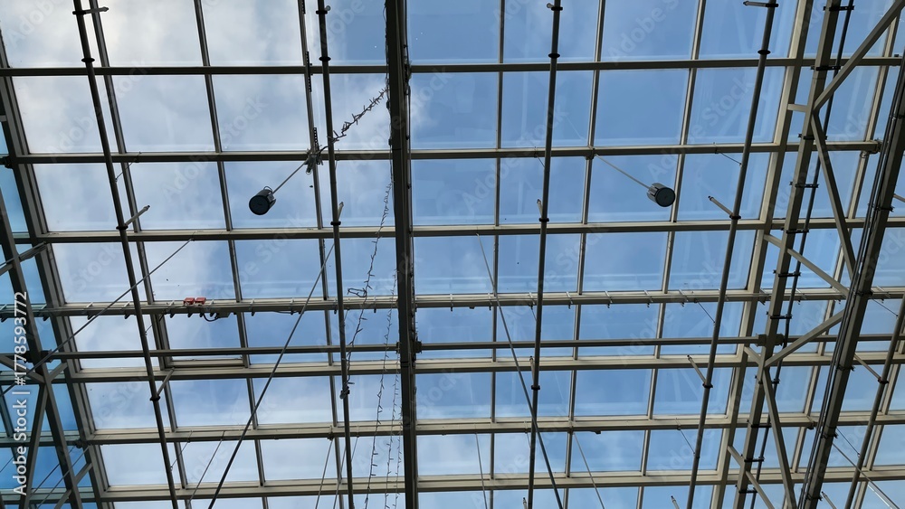 Obraz premium Modern glass and steel roof structure with a clear blue sky and clouds, architectural background for construction, engineering, and design concepts