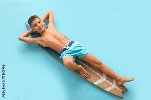 Photography Cute little boy lying on surfing board against blue background