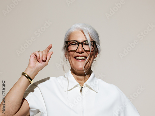 Joyful Older Woman Smiling and Pointing Against a Neutral Background