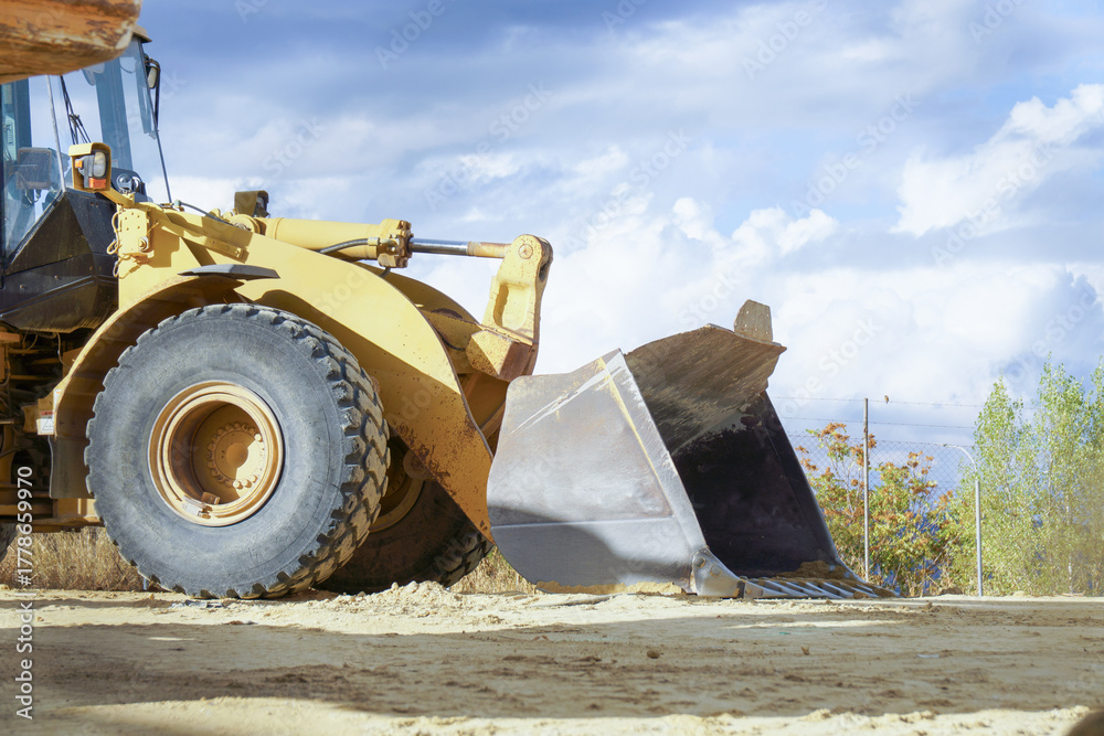 Fototapeta premium ronda,malaga,spain Yellow wheel loader standing on a dusty construction site with a large bucket and heavy tires under a blue sky