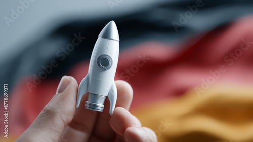 A hand holding a miniature rocket against a blurred German flag background, symbolizing innovation and ambition.