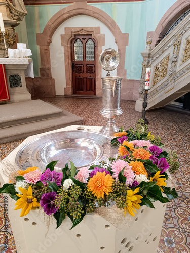 Taufschale und Taufkanne mit Blumen geschmückt in einer Kirche