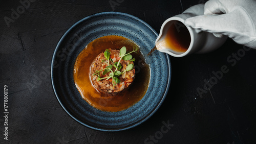 Obraz na plátne Close-up of a gourmet meal served on a blue plate with brown sauce poured from a jug