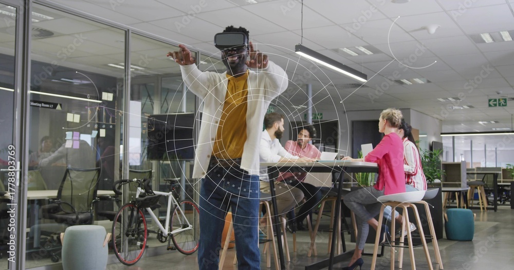 Fototapeta premium Gesturing man wearing VR headset interacting with virtual graphics in office space with bicycle