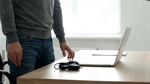 Man standing at desk with laptop and charging cable ready to work.