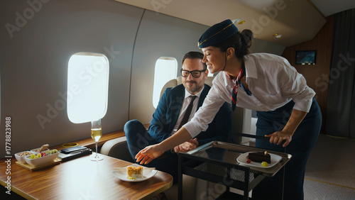 Smiling flight attendant serving a delicious dessert to a male businessman enjoying luxury service and travel in the first class cabin of a private aircraft