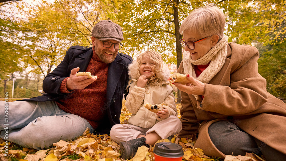 Obraz premium Little girl with father and grandmother sharing laughter while eating pizza outdoors. Concept of family warmth, playfulness, and love for lifestyle, tourism, and food branding visuals.