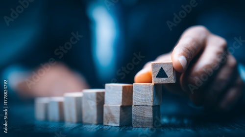 Man placing wooden block with upward arrow on top of stacked blocks in a growth pattern on dark surface