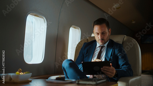 Foto Businessman in a suit focusing on his digital tablet while relaxing on a comfort
