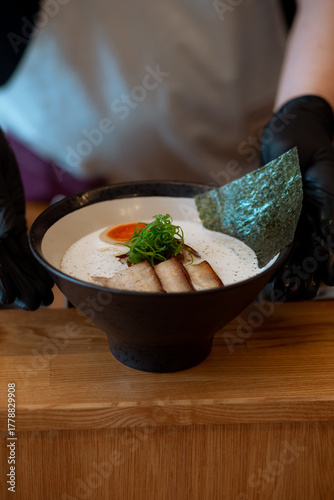 Ramen noodle in intense broth with Chashu pork, fresh green onions and egg in bowl.