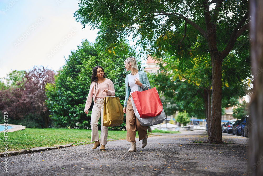 Obraz premium Friends walking through park carrying shopping bags on a sunny day