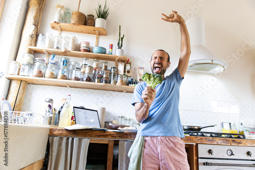 Joyful man enjoying dancing and singing while cooking at home