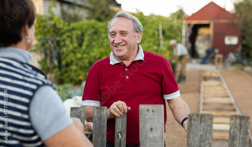 Two gardeners friendly talking outdoors next to wooden fence of country estate on day