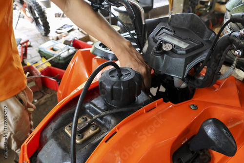 Bild auf Leinwand Focused man doing atv repair and maintenance on an orange vehicle engine in garage