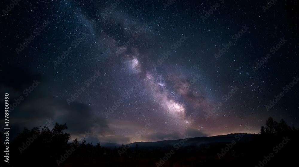 Fototapeta premium The Milky Way galaxy illuminates a dark silhouetted landscape under a vast starry night sky
