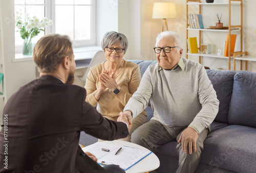 Obraz na płótnie Satisfied senior couple making deal, signing contract or agreement paper, shaking hands with professional agent, financial advisor or medical insurance broker