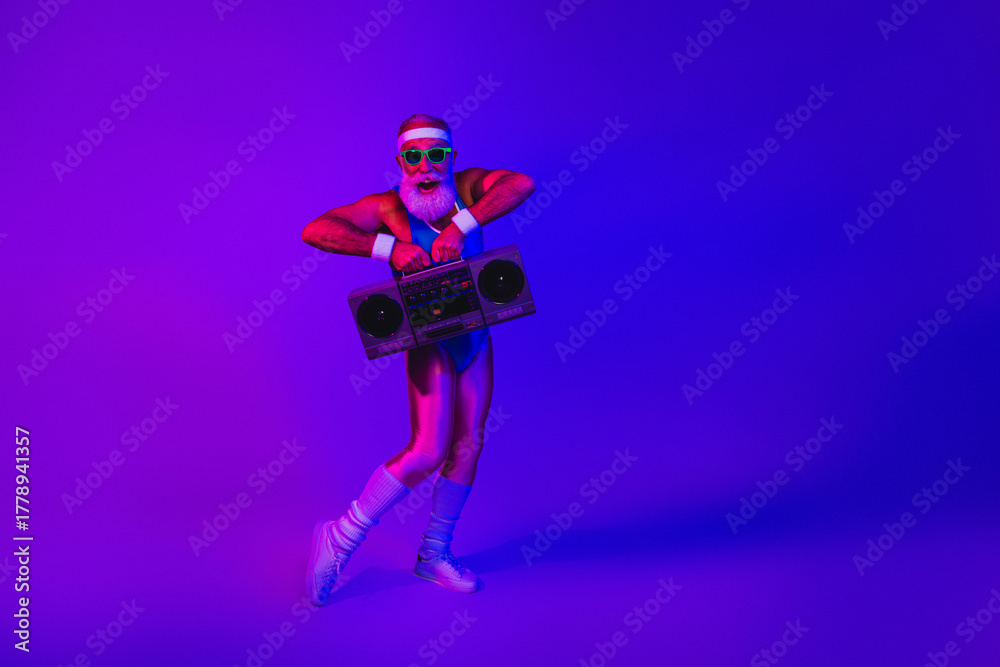 Naklejka premium Elderly man in retro gym outfit with boombox under purple blue neon lights posing for a fitness themed stock image
