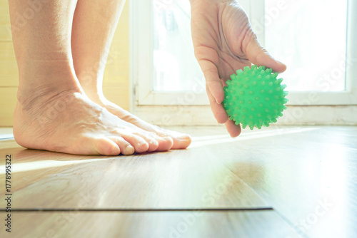 Tablou pe pânză Person gripping a green massage ball near bare feet in natural lighting, close-up